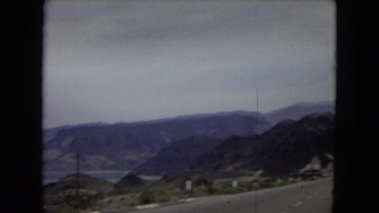 Arizona 1967 home-movie view of rugged desert mountains and a road edge seen through the dark framing of an automobile windshield.