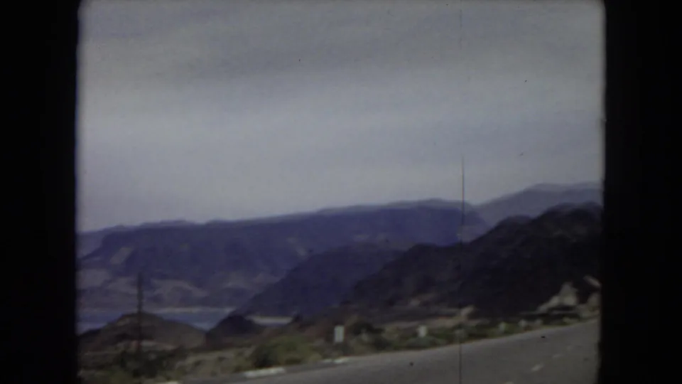Arizona 1967 home-movie view of rugged desert mountains and a road edge seen through the dark framing of an automobile windshield.