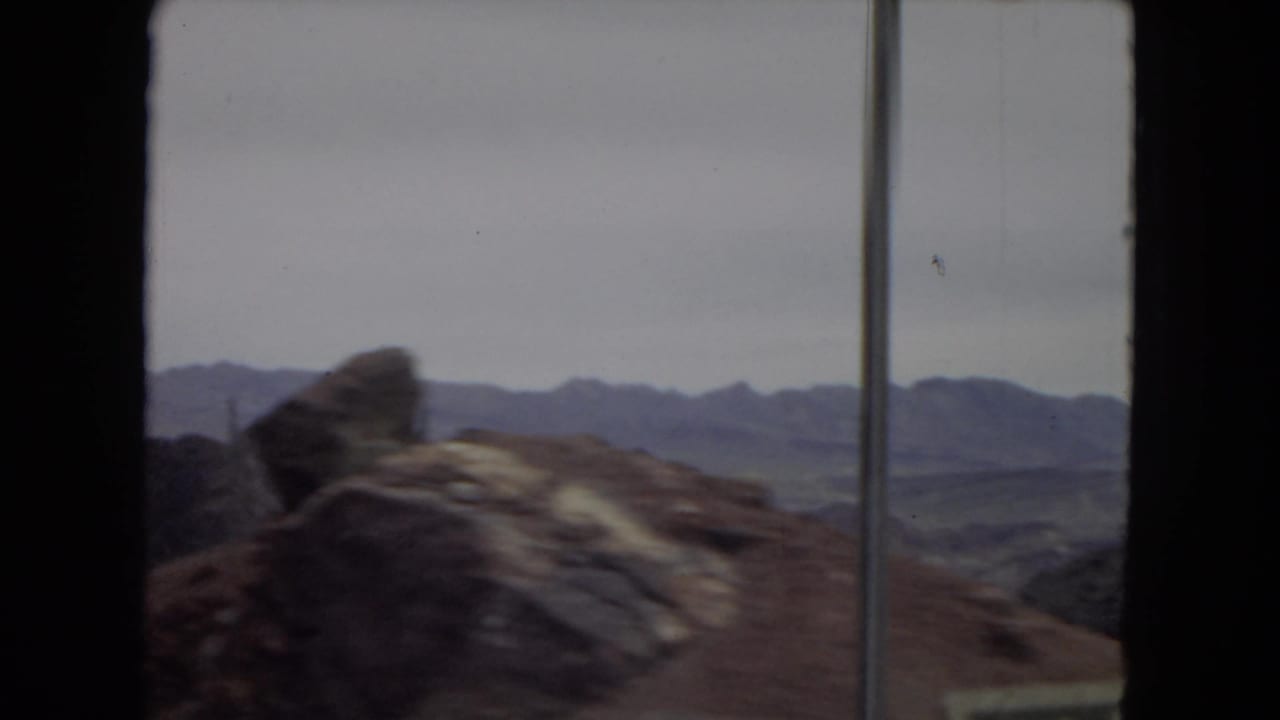 Rock formations and distant mountain ridges in the arid Southwest, filmed from inside a moving vehicle on 8mm home-movie film.
