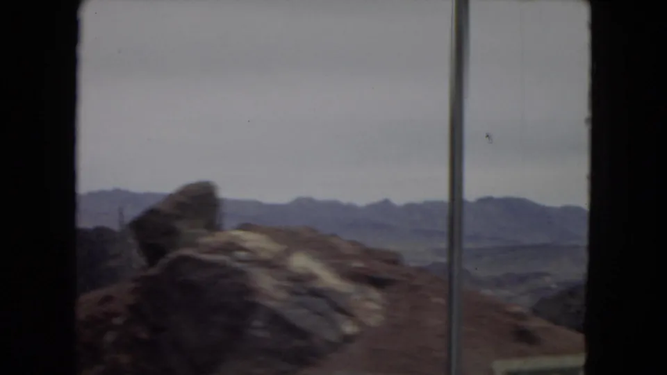 Rock formations and distant mountain ridges in the arid Southwest, filmed from inside a moving vehicle on 8mm home-movie film.