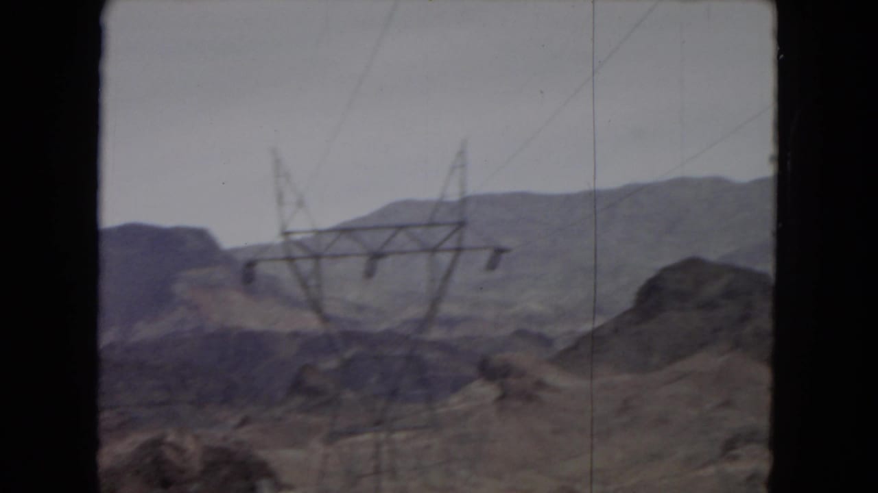 1967 home-movie view of arid hills and distant mountains in the American Southwest, with power transmission towers crossing the landscape.