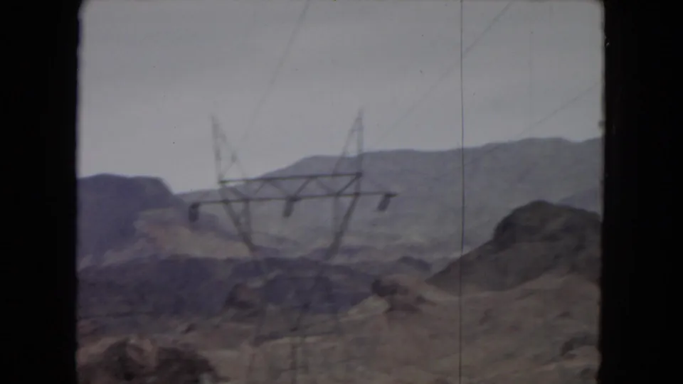 1967 home-movie view of arid hills and distant mountains in the American Southwest, with power transmission towers crossing the landscape.