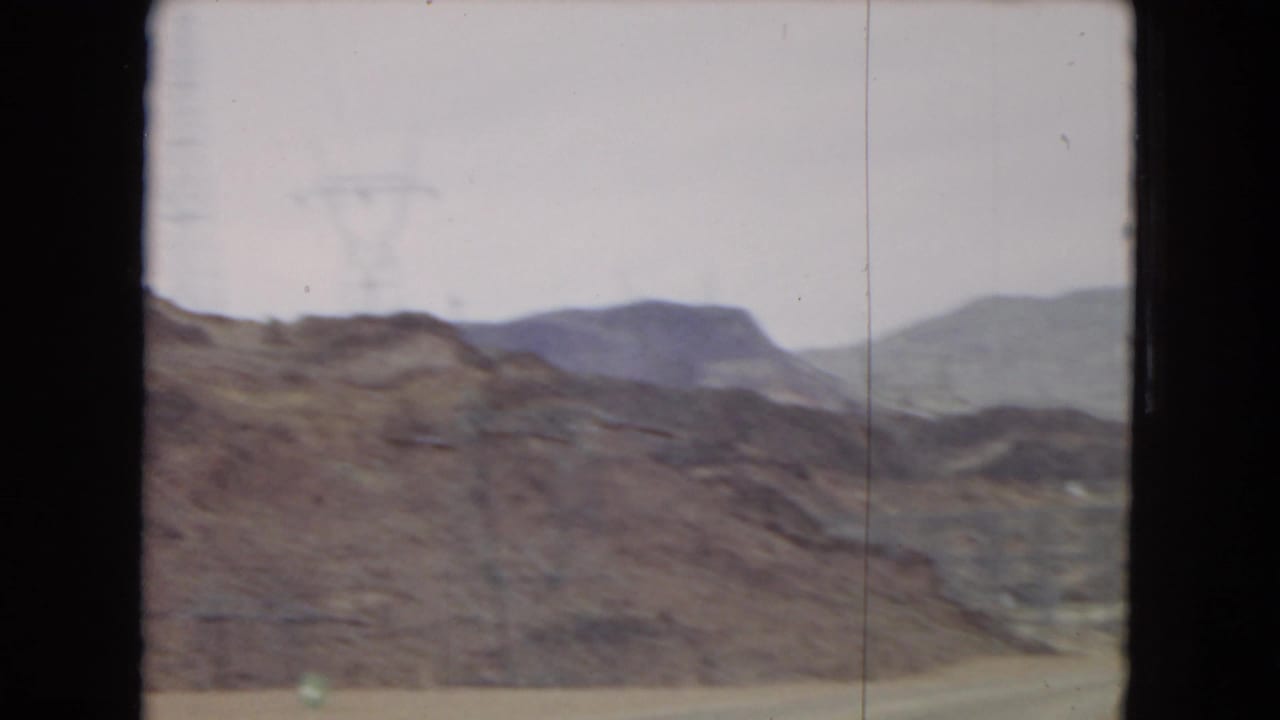 Rocky desert slope with distant mountain ridges under a pale sky.
