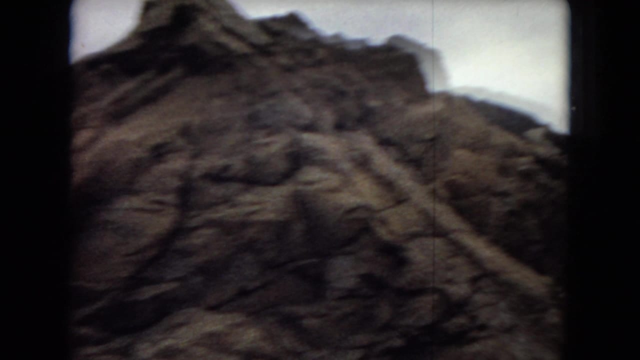 Close view of a craggy rocky mountainside passing near the camera, with dark vehicle-window edges and soft 8mm motion blur.