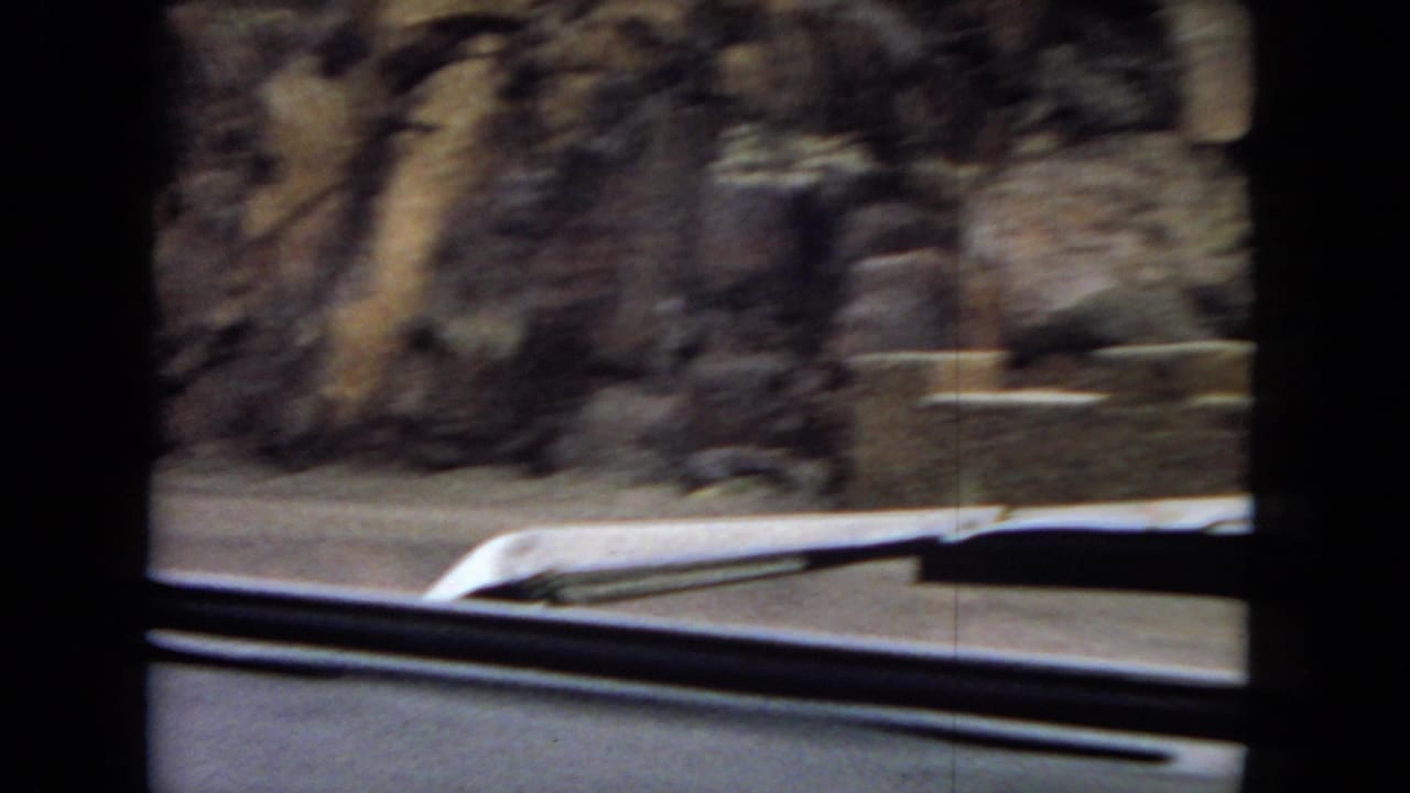 Rocky roadside canyon seen over a car hood and windshield wipers.