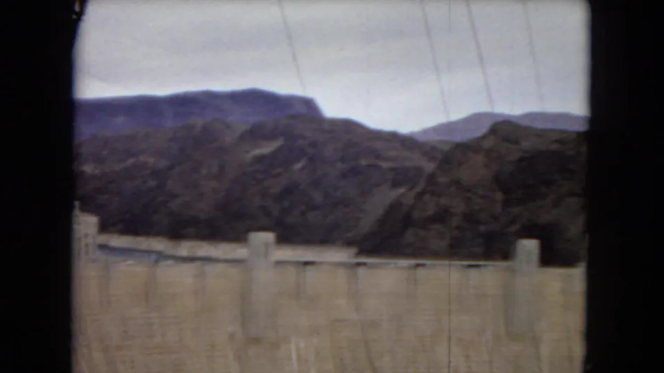 Clearer 1967 8mm frame of Hoover Dam across the lower foreground, backed by rugged desert hills and a pale sky.