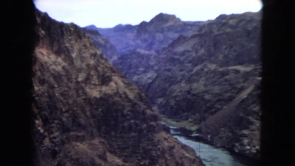 1967 8mm view of a river winding through steep canyon terrain near the supplied Arizona dam setting, with distant mountain ridges in soft focus.