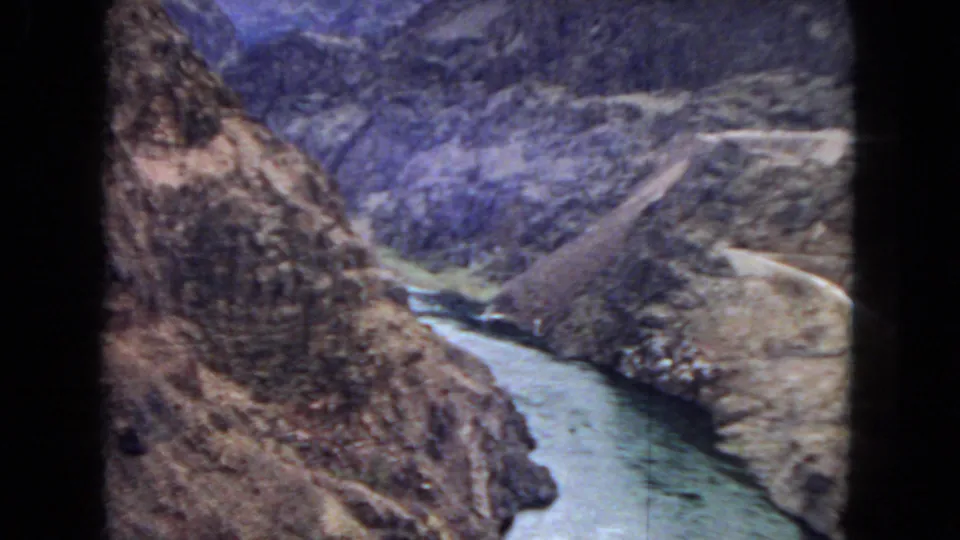 1967 8mm elevated view of the river corridor below rugged canyon slopes, with a pale road-like line or embankment along the right side.