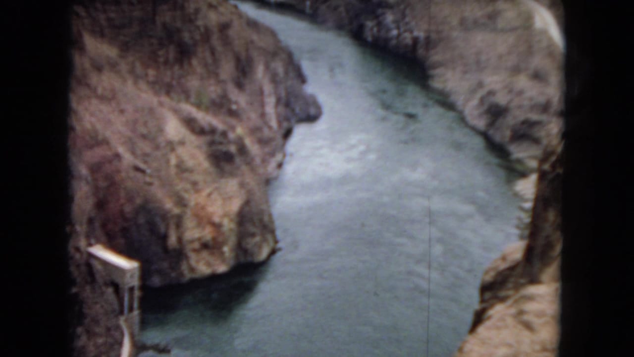 1967 8mm home-movie frame from Arizona showing the river narrowing between rocky canyon walls, with a small dam-like or intake structure visible along the left bank.