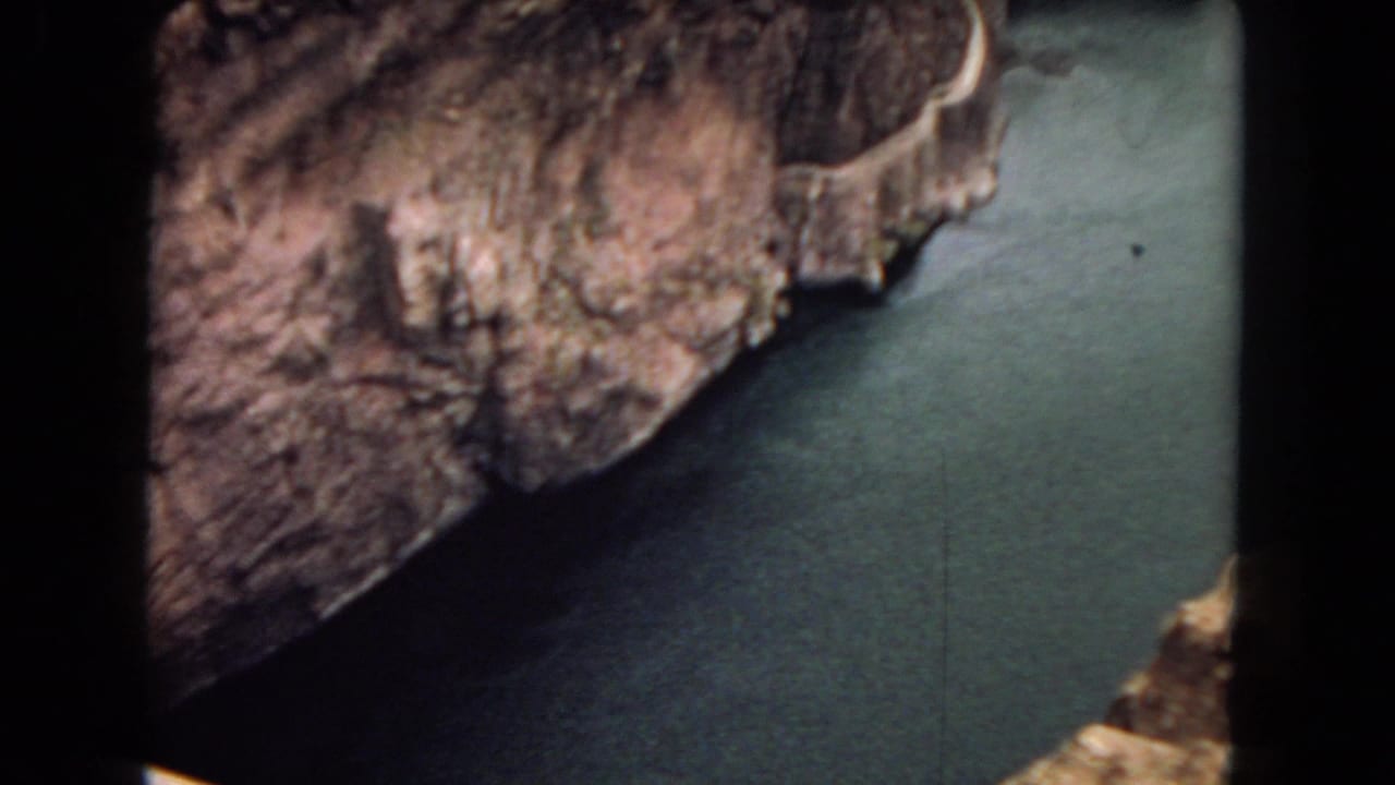 1967 8mm frame showing rugged canyon rock and green-blue river water below, likely near the Hoover Dam area based on clip metadata.