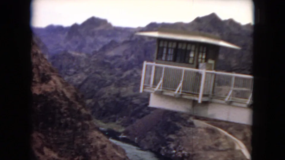 Visitor-shot 8mm view of a white-railed lookout structure projecting over a rugged canyon with the river visible below in the Hoover Dam area.