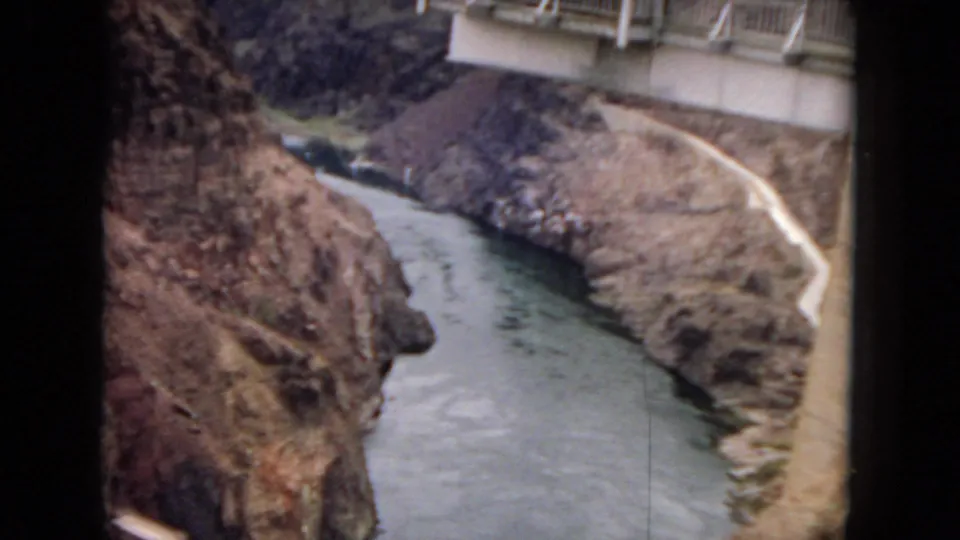 8mm frame looking down into a rocky desert canyon where the river bends below a pale winding road and part of the overlook remains at the top edge.
