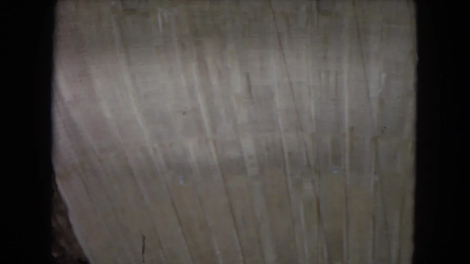 Close 8mm frame of pale unfinished concrete, likely part of the dam, showing vertical texture, film wear, and a small rocky edge near the lower left.