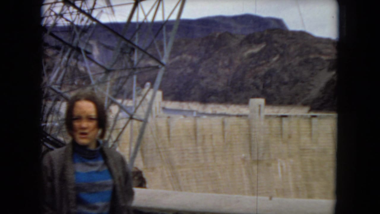 Woman facing the camera in front of Hoover Dam and rocky mountains.