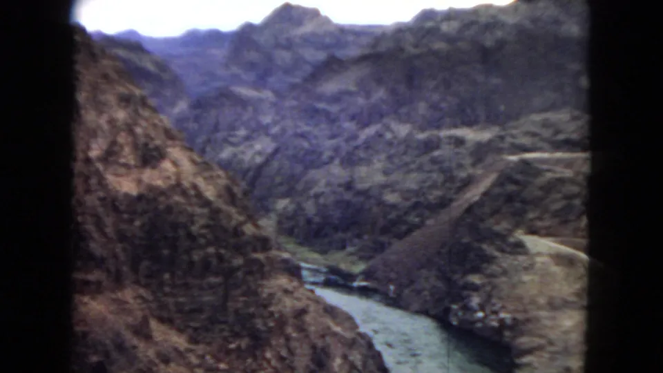 A handheld 8mm view looks down into a rugged canyon where the Colorado River bends between steep rocky slopes under a pale sky.
