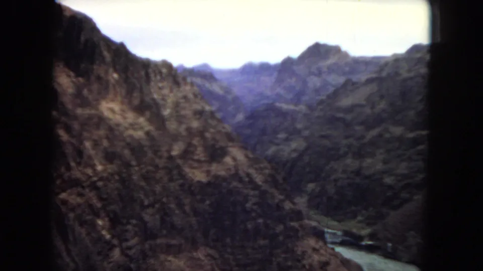 1967 8mm Arizona home-movie frame showing a rugged canyon with steep rock walls and a winding river far below.