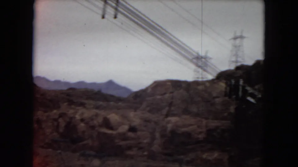 1967 8mm Arizona home-movie frame showing overhead power lines and transmission towers crossing a rugged desert canyon landscape.
