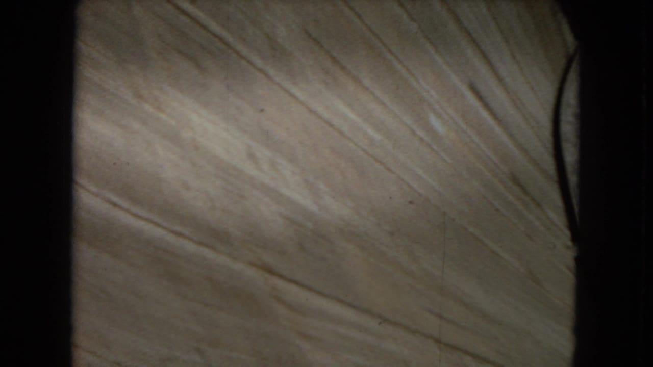 1967 8mm frame showing a close, downward view of pale concrete or dam surface with dark vertical structural edges at the sides.