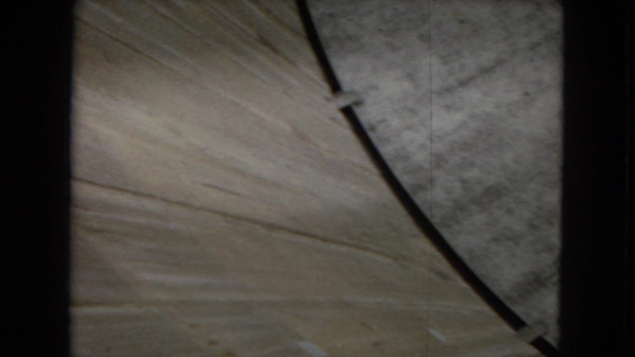 1967 8mm frame looking down at concrete and a dark curved railing or cable near the top of a large dam structure in Arizona, based on clip metadata.