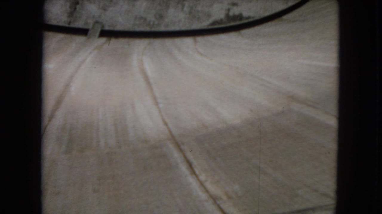 1967 8mm frame showing an elevated view across a pale concrete section of Hoover Dam, bordered by dark film-gate edges and soft home-movie focus.