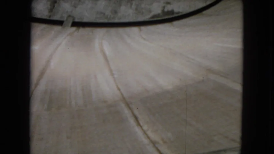 1967 8mm frame showing an elevated view across a pale concrete section of Hoover Dam, bordered by dark film-gate edges and soft home-movie focus.