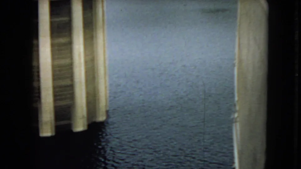 1967 Arizona 8mm frame looking past a vertical concrete dam edge toward a broad calm reservoir surface.