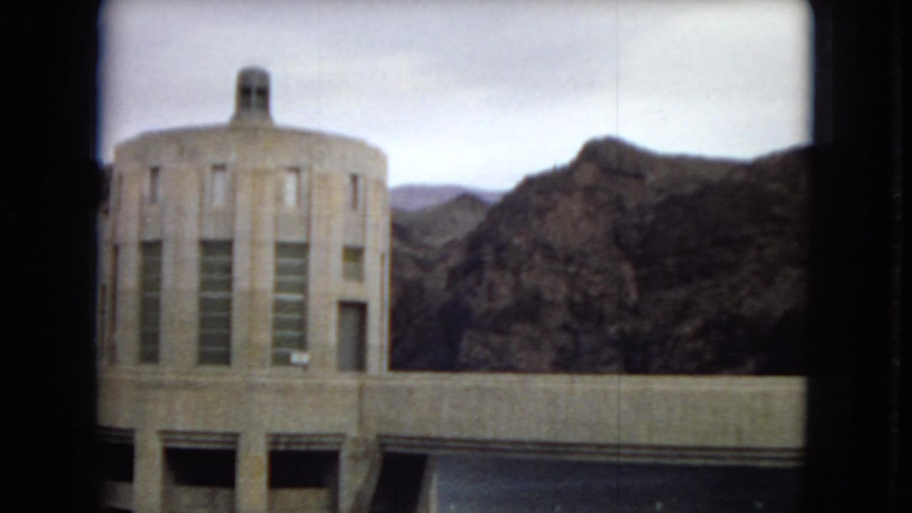 1967 Arizona dam view with a rounded concrete utility building, vertical windows, dam water, and rugged desert hills in the background.