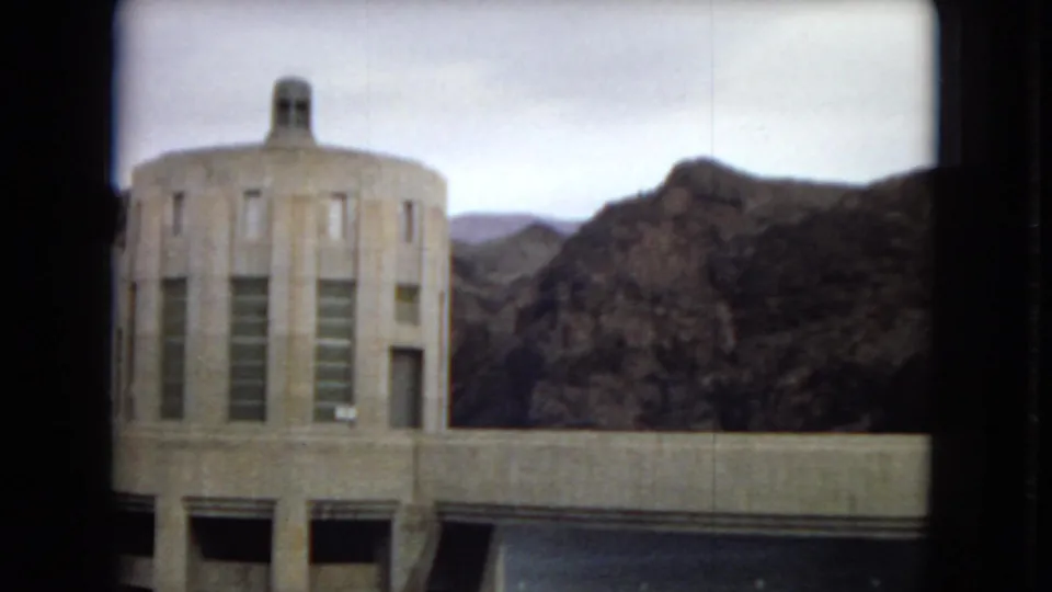 1967 Arizona dam view with a rounded concrete utility building, vertical windows, dam water, and rugged desert hills in the background.