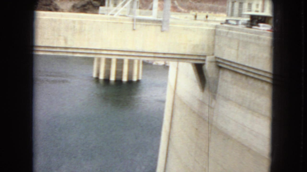 Concrete dam wall and reservoir water seen from close range with structural supports above the water.