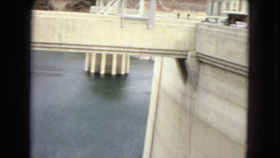 Close visitor-shot view of a large concrete dam face, reservoir water, and bridge-like supports in the Arizona dam setting described by the clip metadata.