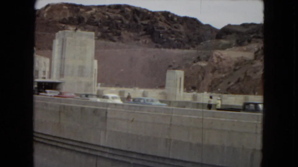 A visitor-level 1967 view shows parked cars, concrete dam structures, roadway barriers, and rugged hills around Hoover Dam.