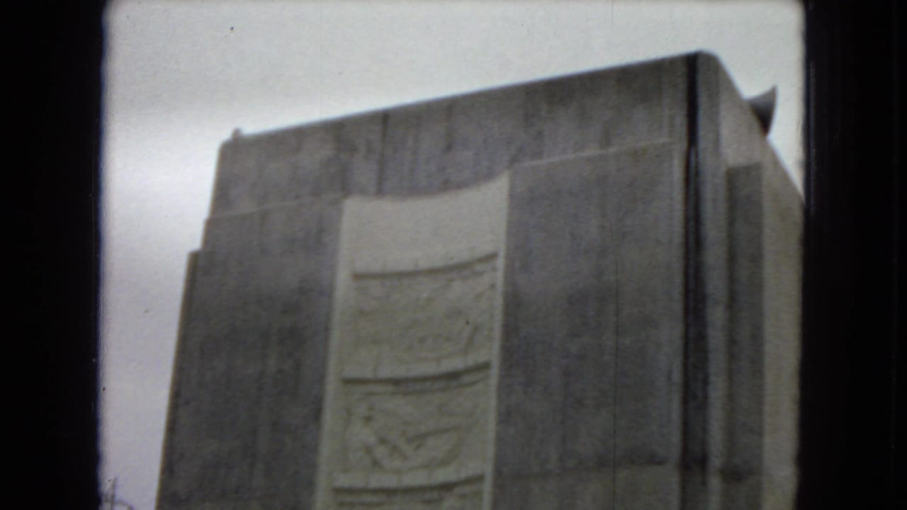 1967 Arizona home-movie frame showing a large concrete dam wall or tower with a recessed decorative panel, filmed from a low visitor viewpoint.