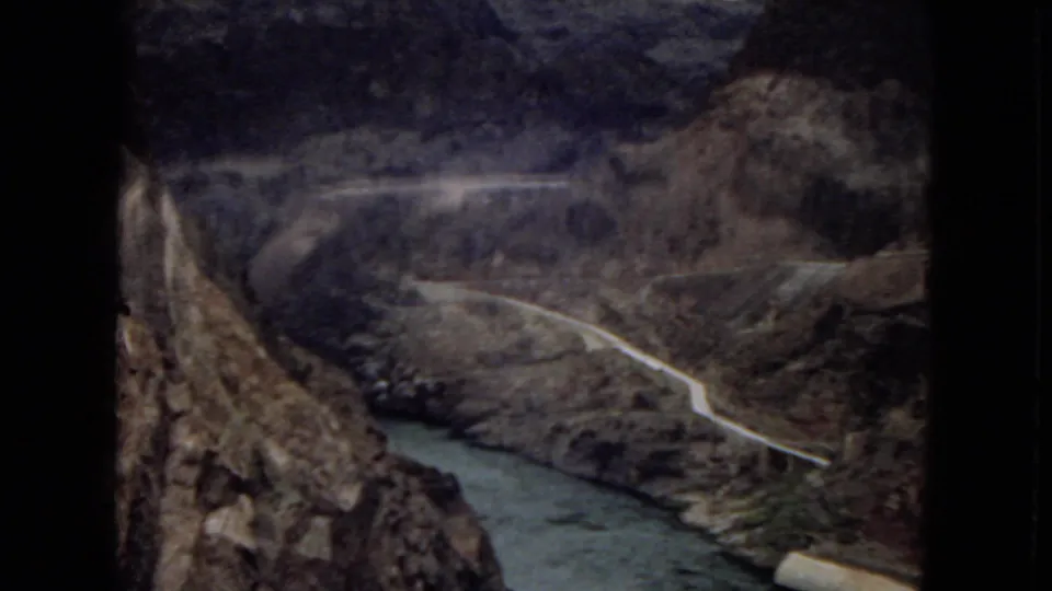 1967 Arizona home-movie frame showing a canyon view with a winding river, steep rocky slopes, and a road tracing the landscape below.