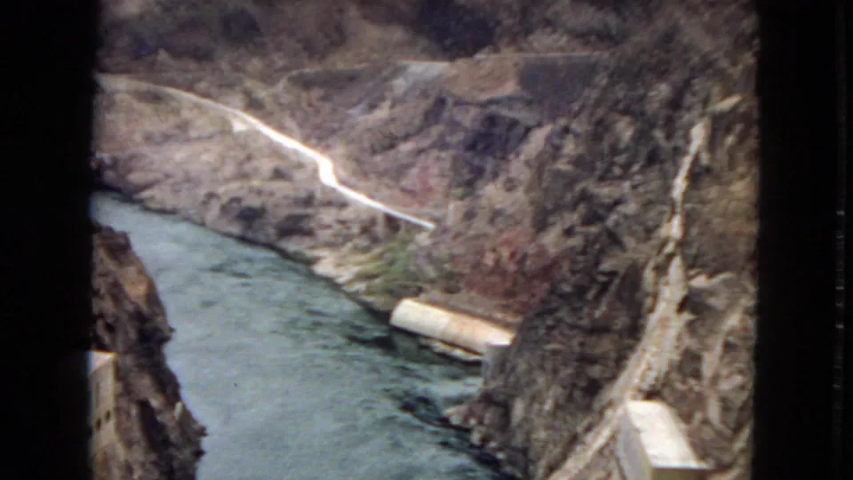 1967 8mm Arizona view looking down on blue-green canyon water, a pale road, rock walls, and a concrete tunnel or portal near the river.