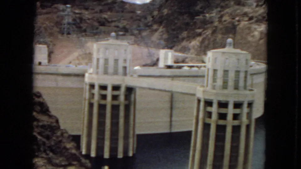 Visitor-shot 8mm frame of Hoover Dam or Boulder Dam in Arizona, with tall intake towers, the curved concrete structure, reservoir water, and desert canyon walls.