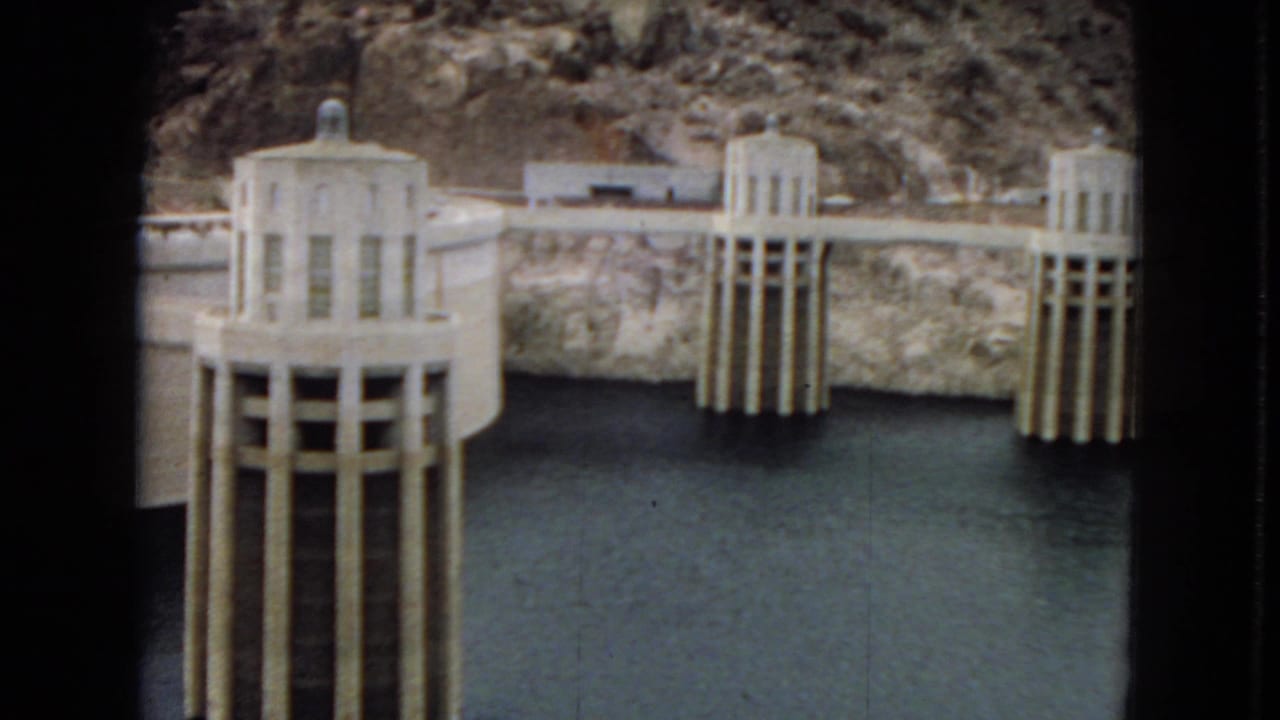 1967 8mm view of Hoover Dam intake towers rising from reservoir water against steep canyon walls.