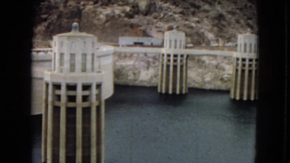 1967 8mm view of Hoover Dam intake towers rising from reservoir water against steep canyon walls.