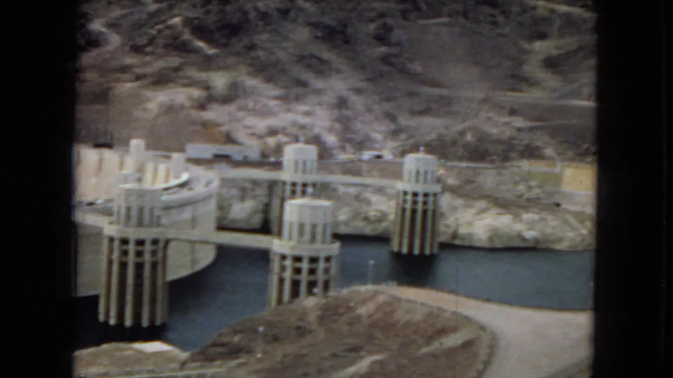 Final 1967 home-movie frame showing Hoover Dam intake towers across dark water, with concrete structures and arid canyon slopes in the background.