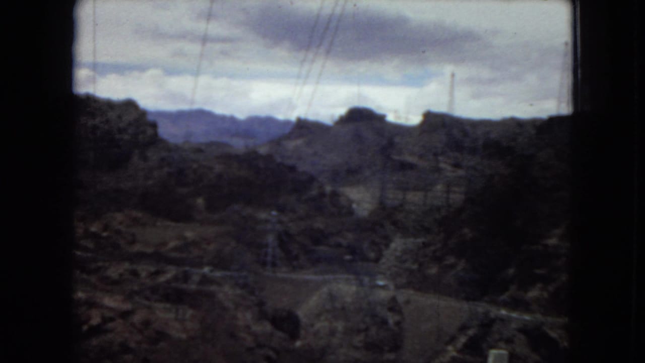 1967 8mm footage shows a dark, grainy view across desert canyon terrain with power lines and distant mountains, likely filmed from a moving vehicle in the American Southwest.