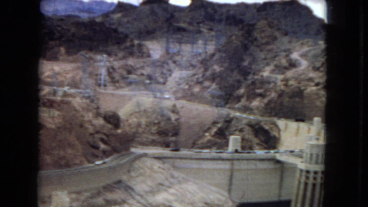 A concrete dam structure, appearing to be Hoover Dam based on the clip metadata, sits between rocky canyon walls with roads and utility infrastructure visible around it.