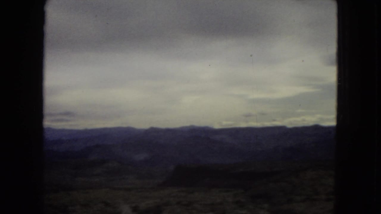 1967 archival 8mm view of broad Southwest mountain terrain under heavy cloud, filmed from inside or near a moving vehicle.