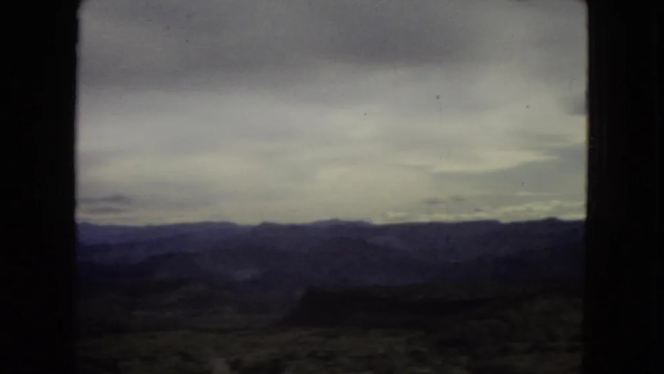 1967 archival 8mm view of broad Southwest mountain terrain under heavy cloud, filmed from inside or near a moving vehicle.