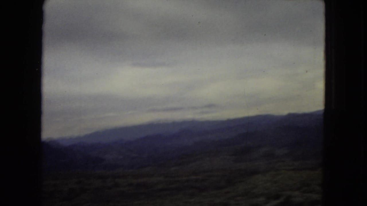 Archival home-movie frame showing layered mountain slopes and an overcast sky during a 1967 Southwest road journey.