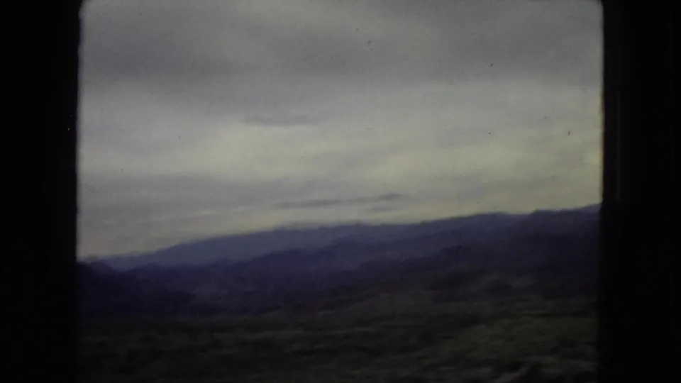 Archival home-movie frame showing layered mountain slopes and an overcast sky during a 1967 Southwest road journey.