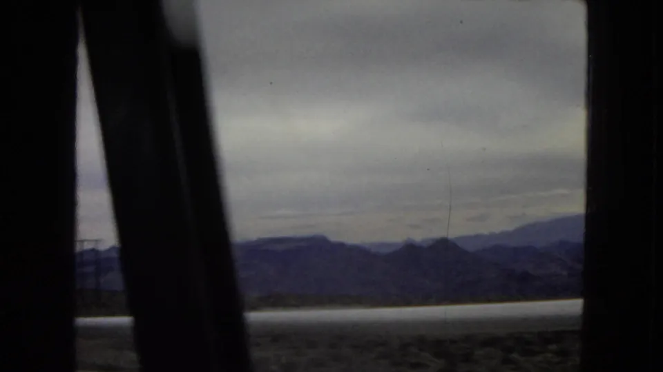 1967 8mm travel view of distant mountains and open land, partially obstructed by the dark edge of a vehicle window.