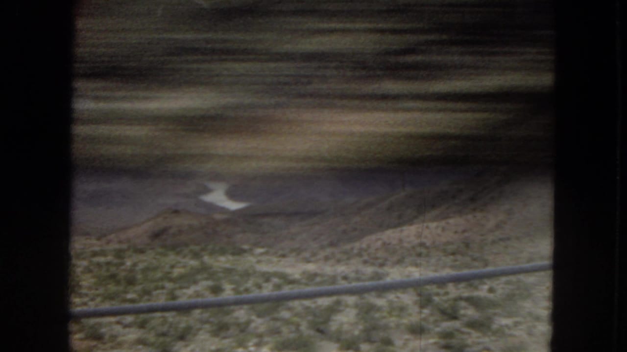 Blurred desert hillside, railing, and winding water below the mountains.