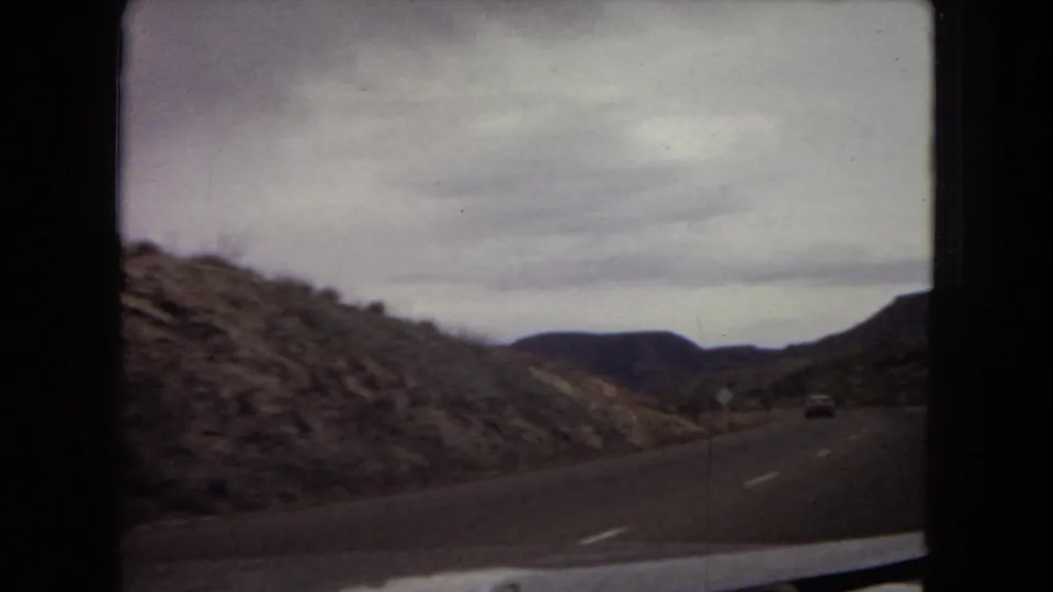 1967 Arizona driving view showing a curving highway through rugged desert hills, filmed from inside a moving car.