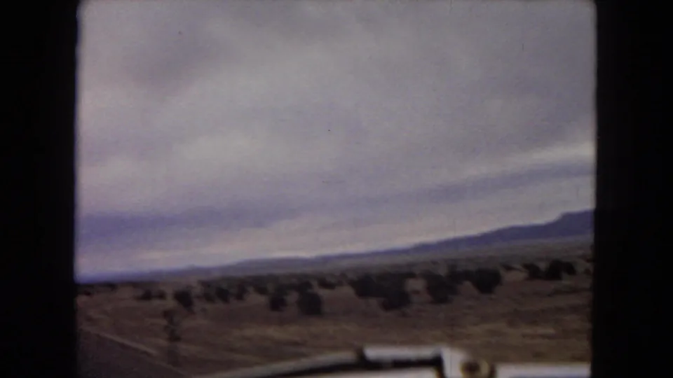 1967 Arizona 8mm frame with a soft, moving-car view across desert scrub toward low mountains beneath an overcast sky.