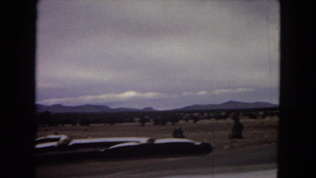 Roadside desert landscape with distant mountains and the car roofline visible at the bottom.
