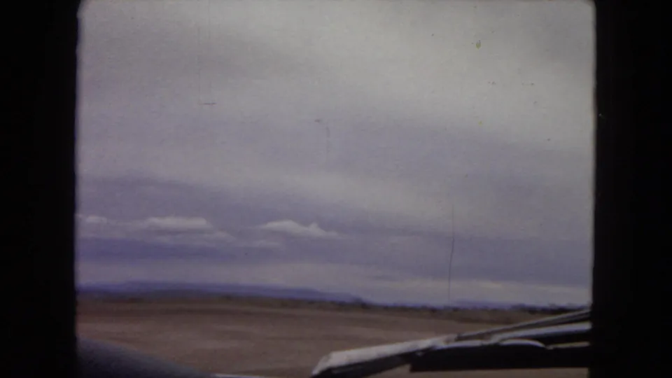 1967 Arizona desert horizon and cloudy sky filmed from inside or beside a moving car, with a portion of the vehicle visible along the lower frame.